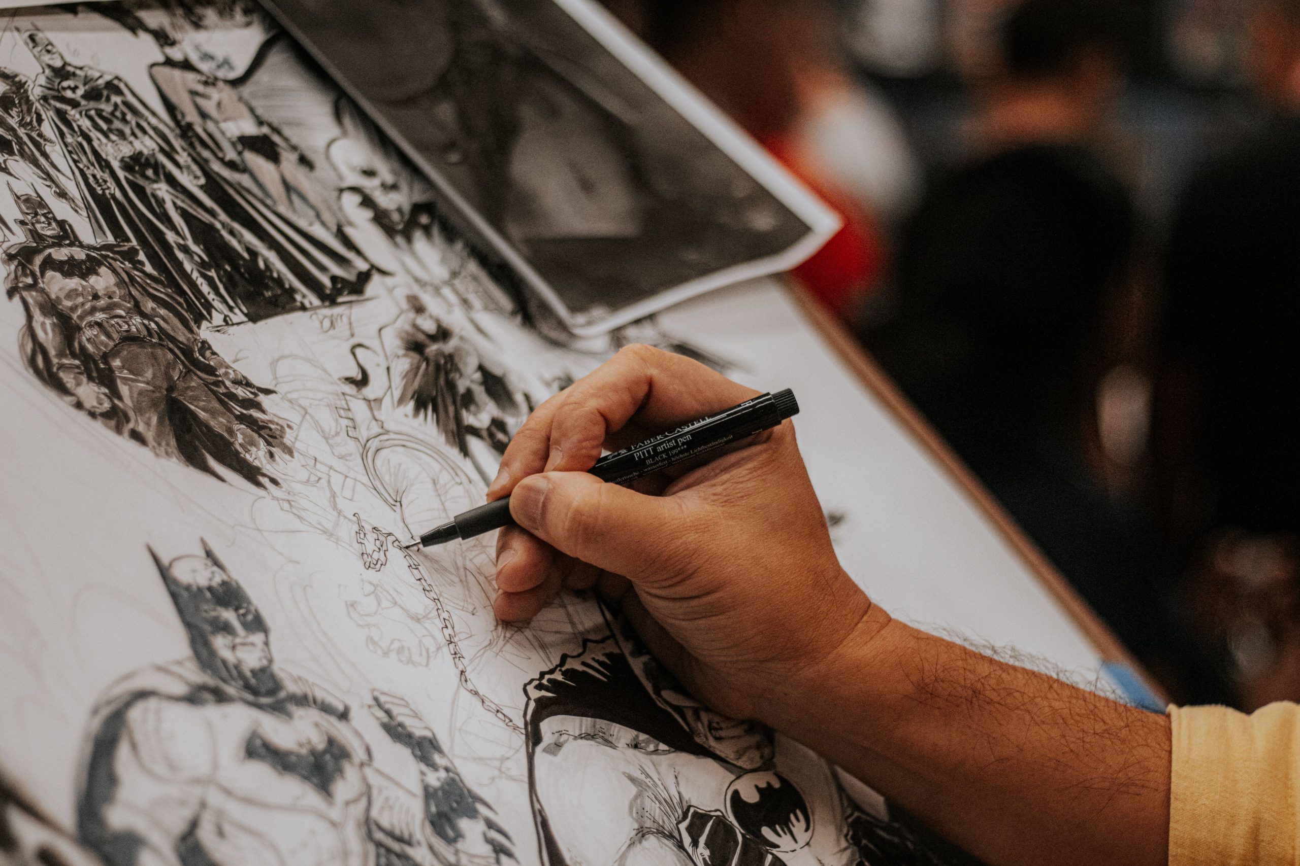 comic-artist-drawing-human-illustration Human comic artist drawing detailed comic book characters with a pen, representing traditional illustration craft